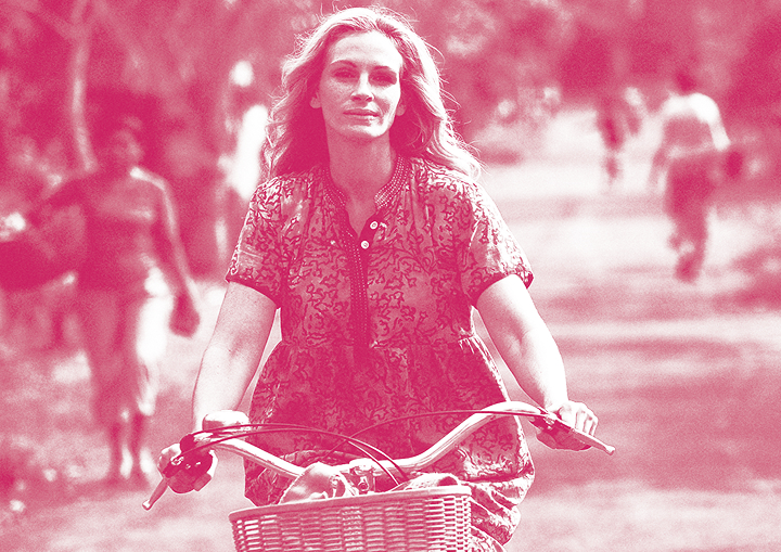 Woman in a patterned dress bikes toward the camera on a park path, blurred pedestrians in the background.